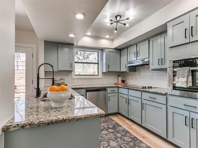 kitchen with stainless steel appliances, a sink, under cabinet range hood, and gray cabinetry