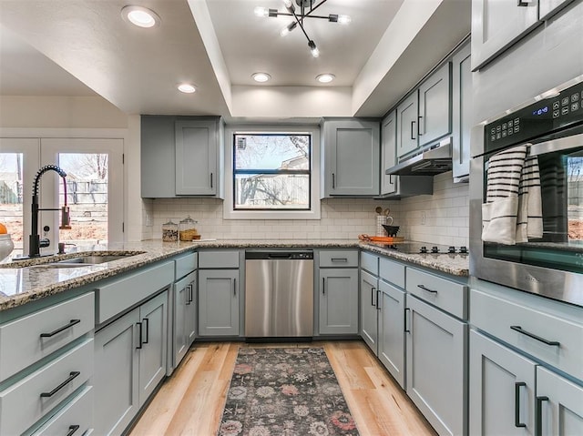 kitchen featuring stainless steel appliances, gray cabinets, light wood-style flooring, a sink, and under cabinet range hood