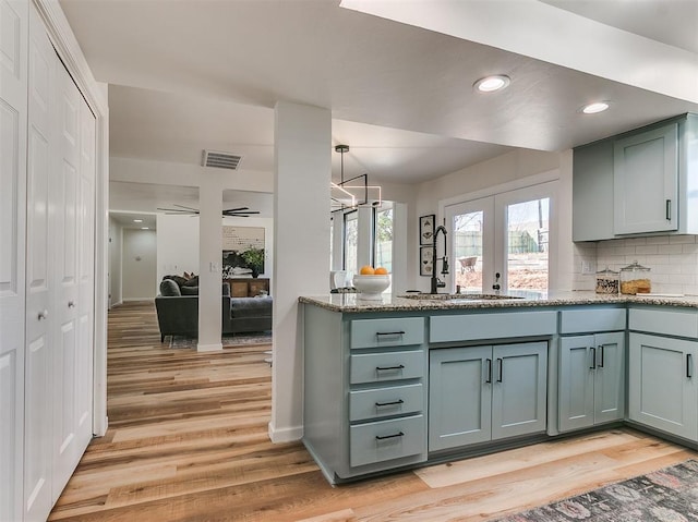 kitchen with visible vents, decorative backsplash, a sink, light stone countertops, and light wood-type flooring