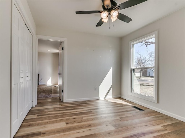 empty room with a ceiling fan, light wood-type flooring, visible vents, and baseboards