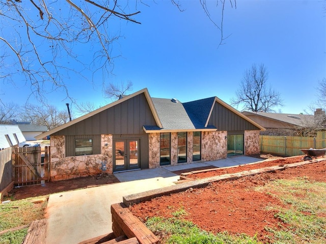 back of house featuring fence, stone siding, french doors, board and batten siding, and a patio area