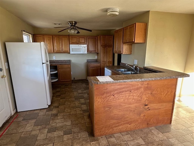 kitchen featuring brown cabinets, a peninsula, white appliances, a ceiling fan, and a sink