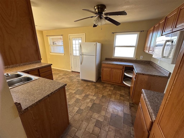 kitchen with brown cabinets, a sink, dark countertops, built in desk, and white appliances