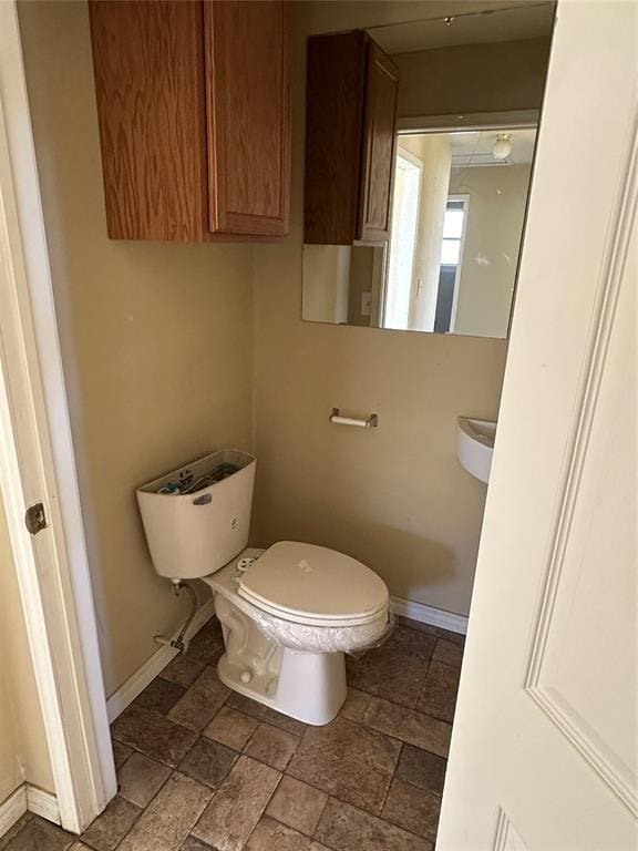 half bath featuring toilet, baseboards, and stone finish flooring