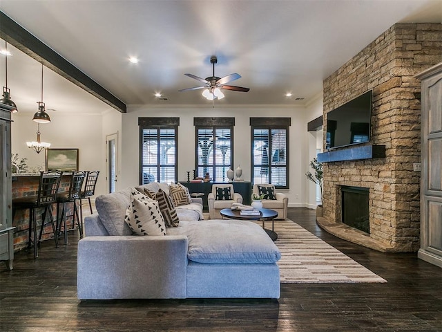 living room featuring ceiling fan with notable chandelier, a fireplace, baseboards, ornamental molding, and dark wood finished floors