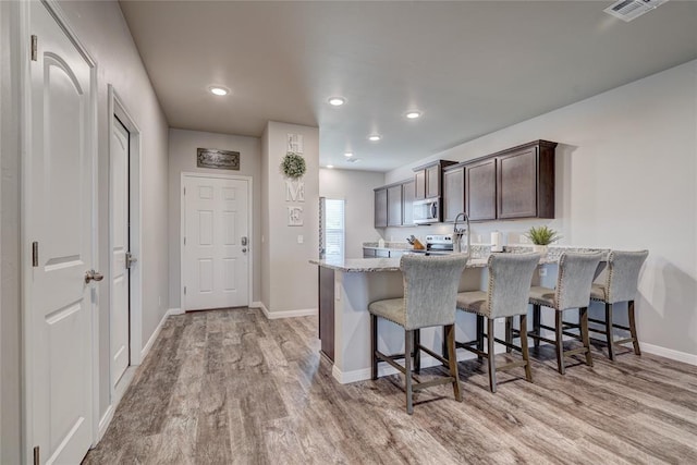 kitchen with a breakfast bar area, stainless steel microwave, light wood-style flooring, dark brown cabinets, and baseboards