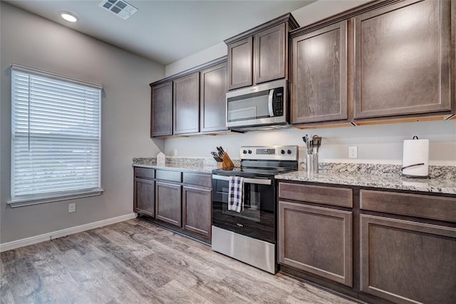 kitchen featuring light wood finished floors, visible vents, appliances with stainless steel finishes, light stone countertops, and dark brown cabinets