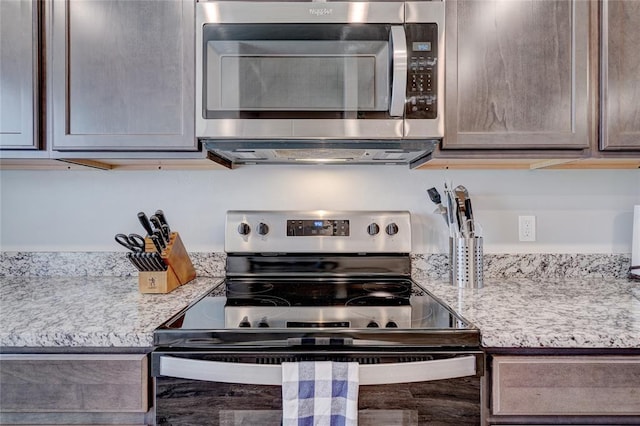 kitchen with stainless steel microwave, range with electric cooktop, and light stone countertops