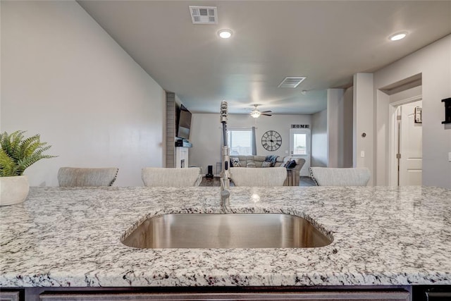 kitchen featuring light stone countertops, a ceiling fan, visible vents, and a sink