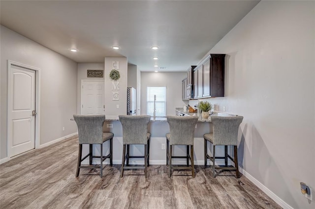 kitchen featuring light wood-style flooring, stainless steel microwave, a peninsula, and a kitchen bar