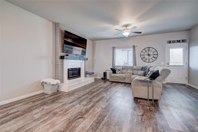 living area featuring ceiling fan, a fireplace, baseboards, and wood finished floors