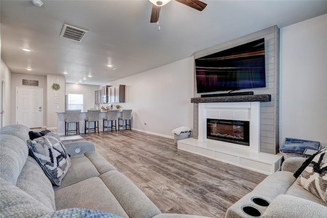 living area featuring a fireplace, wood finished floors, a ceiling fan, visible vents, and baseboards