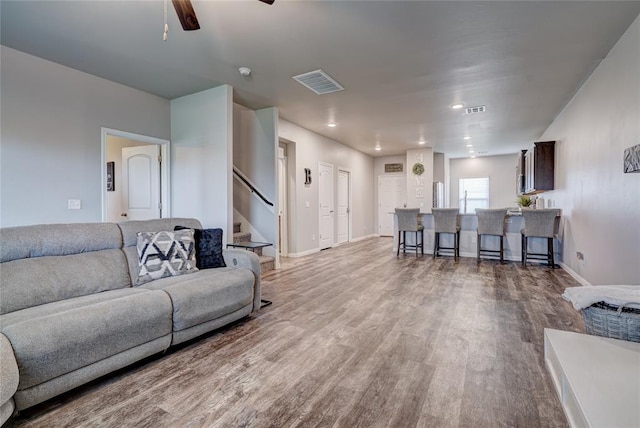 living room featuring baseboards, stairs, visible vents, and wood finished floors