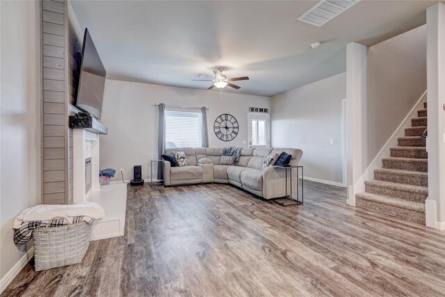 living room with a fireplace with raised hearth, ceiling fan, wood finished floors, baseboards, and stairs