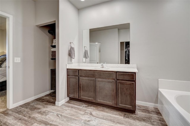 bathroom with a washtub, vanity, baseboards, and wood finished floors