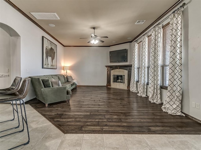 living room featuring visible vents, a fireplace, a ceiling fan, and ornamental molding