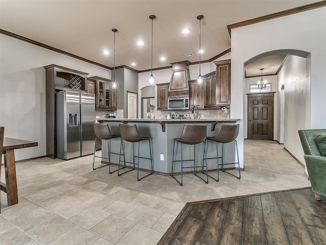 kitchen featuring a kitchen bar, tasteful backsplash, arched walkways, appliances with stainless steel finishes, and dark brown cabinets