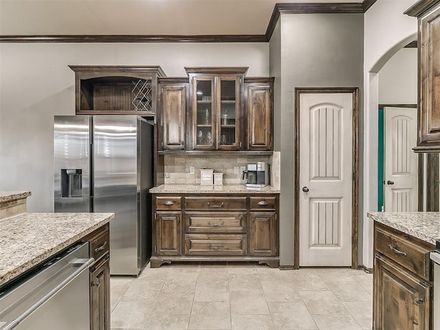 kitchen with decorative backsplash, stainless steel appliances, dark brown cabinetry, crown molding, and glass insert cabinets