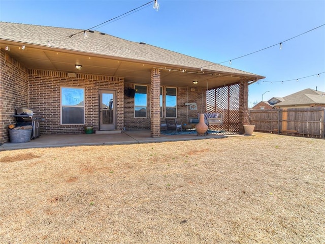 rear view of house featuring brick siding, roof with shingles, a patio, and fence