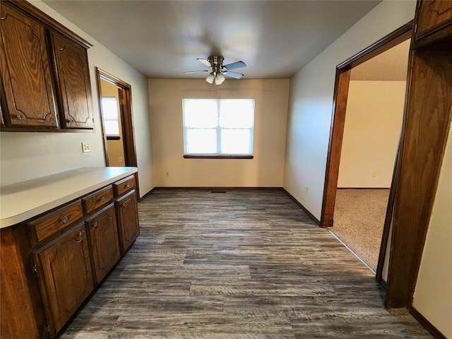 interior space featuring light countertops, dark wood finished floors, a ceiling fan, and baseboards