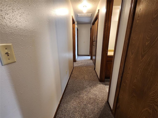 hallway featuring baseboards, visible vents, a textured wall, light colored carpet, and a textured ceiling