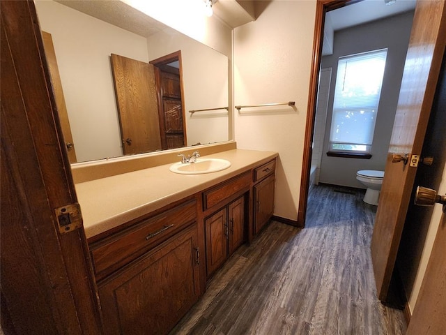 full bath with toilet, vanity, wood finished floors, baseboards, and a bath