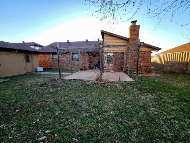 back of house with brick siding, fence, a lawn, a chimney, and a patio area