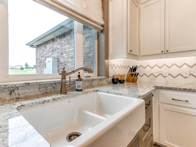 kitchen featuring backsplash, white cabinets, light stone counters, and a sink