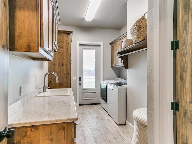 washroom with baseboards, light wood-style flooring, separate washer and dryer, cabinet space, and a sink