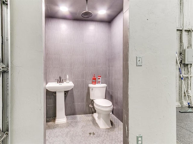 bathroom with a textured wall, toilet, tile walls, and tile patterned flooring