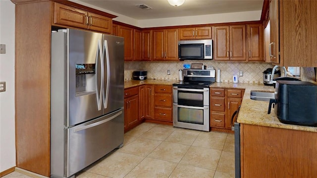 kitchen with light tile patterned floors, visible vents, light stone countertops, stainless steel appliances, and backsplash