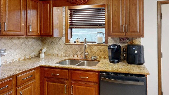 kitchen with light stone counters, a sink, and dishwashing machine