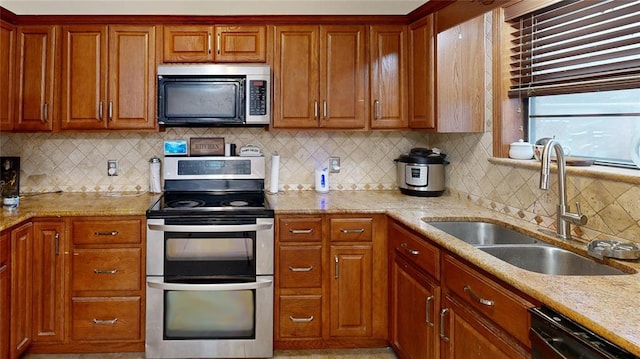 kitchen with range with two ovens, light stone counters, a sink, black dishwasher, and brown cabinets