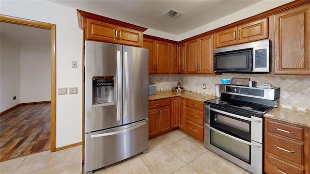 kitchen featuring stainless steel appliances, visible vents, brown cabinetry, and backsplash