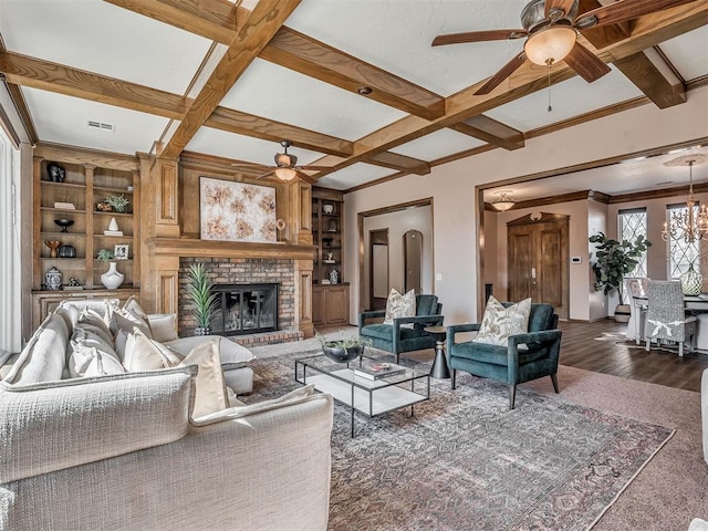 living room with built in shelves, beam ceiling, a fireplace, coffered ceiling, and ceiling fan with notable chandelier