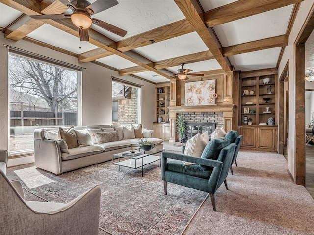 carpeted living room featuring built in shelves, coffered ceiling, a fireplace, a ceiling fan, and beam ceiling