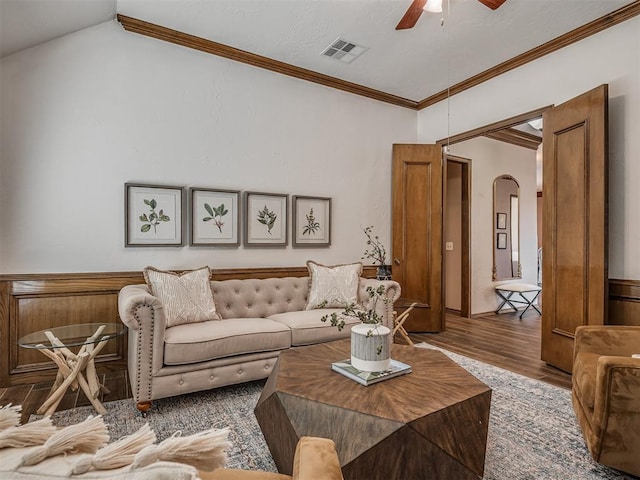 living area with arched walkways, visible vents, ornamental molding, ceiling fan, and wood finished floors