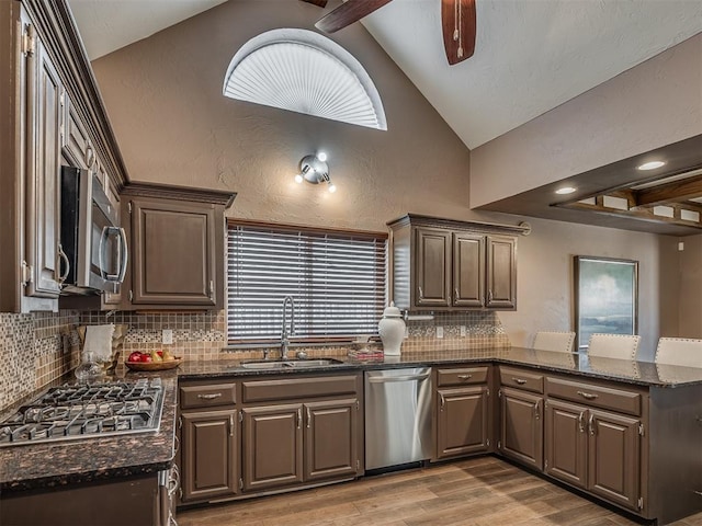 kitchen featuring stainless steel appliances, a peninsula, a sink, vaulted ceiling, and light wood finished floors