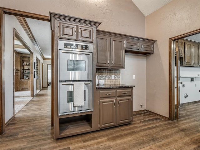 kitchen featuring ornamental molding, stainless steel double oven, dark wood finished floors, and a textured wall