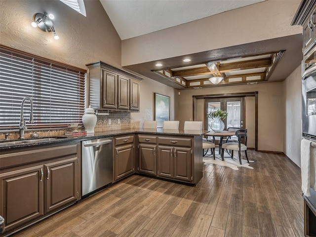 kitchen with a peninsula, a sink, backsplash, dishwasher, and dark wood finished floors