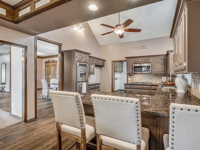 kitchen featuring appliances with stainless steel finishes, dark countertops, dark wood finished floors, and tasteful backsplash