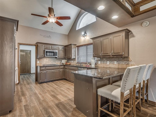 kitchen with a breakfast bar, a peninsula, stainless steel appliances, light wood-style floors, and backsplash