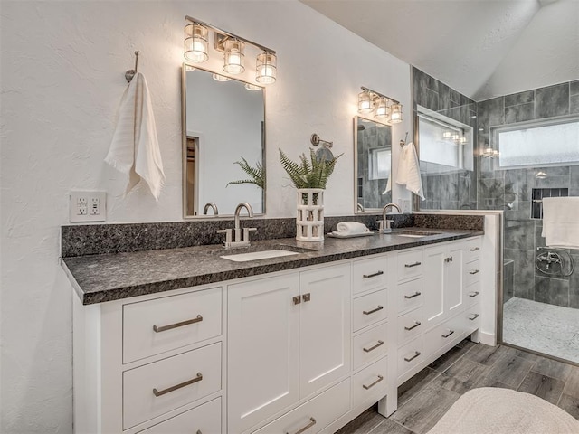 bathroom featuring wood finished floors, double vanity, a sink, and a walk in shower