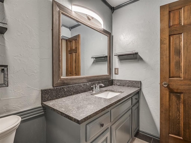 bathroom featuring a textured wall, vanity, and toilet