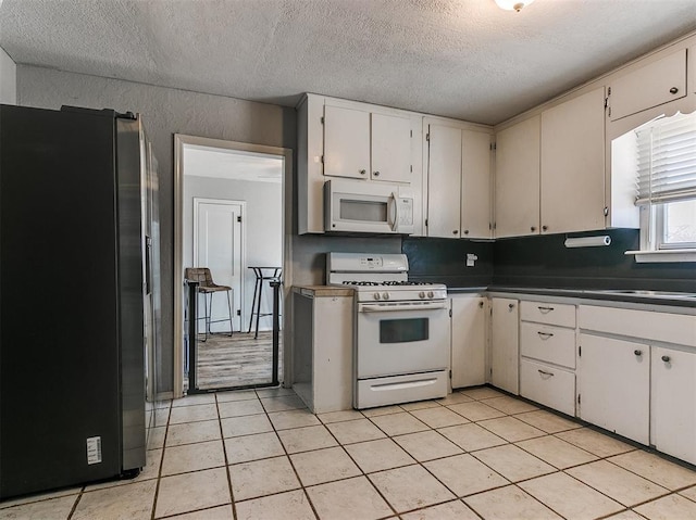 420 W Lincoln St, Purcell, OK 73080 - kitchen with light tile patterned floors, dark countertops, white cabinets, a textured ceiling, and white appliances