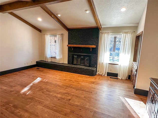 unfurnished living room featuring lofted ceiling with beams, a healthy amount of sunlight, a fireplace, and a textured ceiling