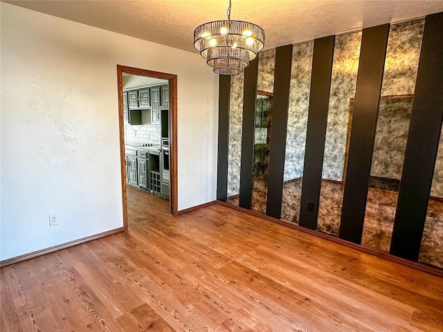 unfurnished dining area with a notable chandelier, a textured ceiling, baseboards, and wood finished floors