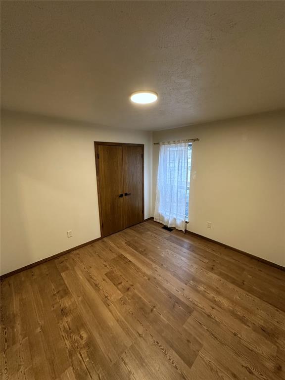 unfurnished bedroom with baseboards, visible vents, wood finished floors, a textured ceiling, and a closet