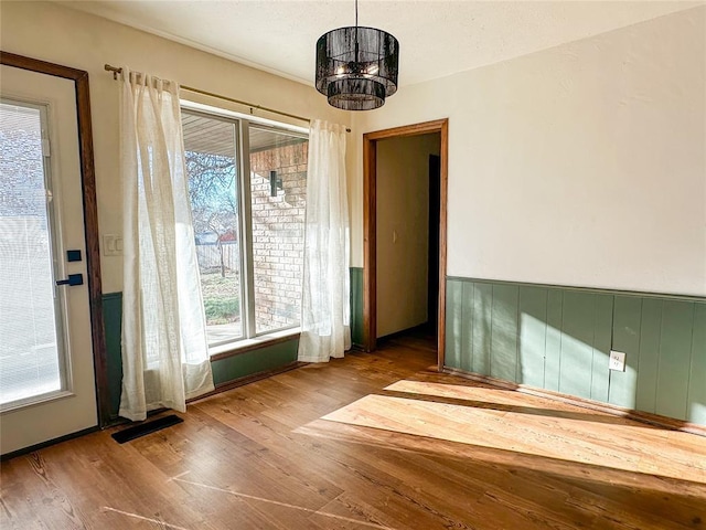 unfurnished dining area with a wainscoted wall, wood finished floors, visible vents, and a notable chandelier