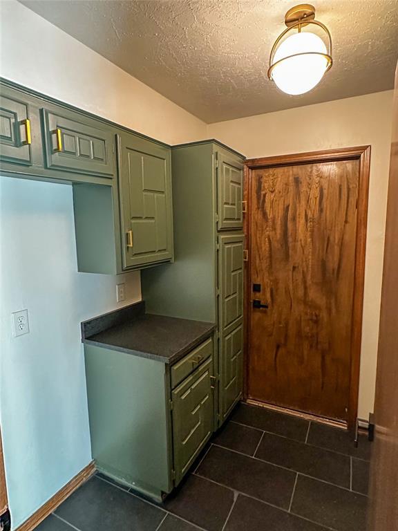 kitchen featuring dark countertops, dark tile patterned floors, green cabinetry, and a textured ceiling